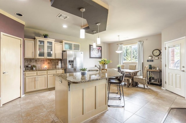 17425 White Hawk Dr, Edmond, OK 73012 - kitchen with stainless steel fridge with ice dispenser, decorative backsplash, a center island with sink, light stone countertops, and light tile patterned floors