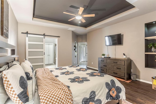 17425 White Hawk Dr, Edmond, OK 73012 - bedroom featuring a tray ceiling, a barn door, wood finished floors, and a ceiling fan