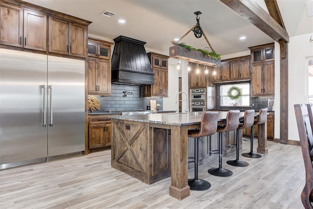 8960 N Banner Rd, Yukon, OK 73099 - kitchen featuring stainless steel appliances, custom exhaust hood, light wood-style floors, backsplash, and glass insert cabinets