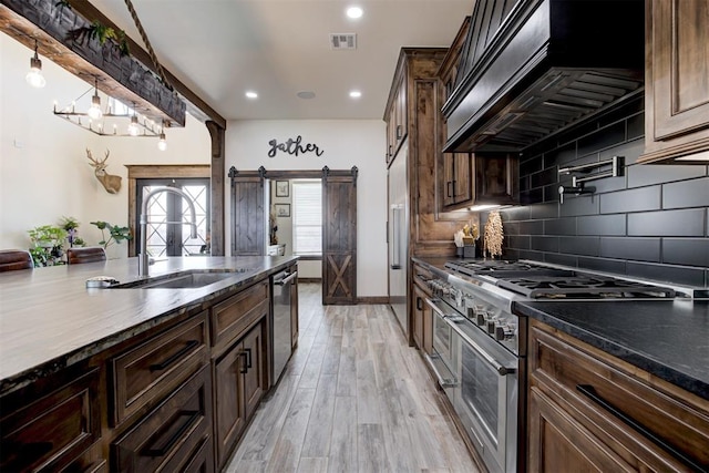 8960 N Banner Rd, Yukon, OK 73099 - kitchen featuring appliances with stainless steel finishes, custom range hood, a barn door, tasteful backsplash, and light wood-style flooring