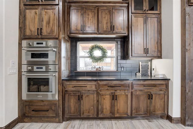 8960 N Banner Rd, Yukon, OK 73099 - kitchen with double oven, dark countertops, light wood-style flooring, backsplash, and glass insert cabinets