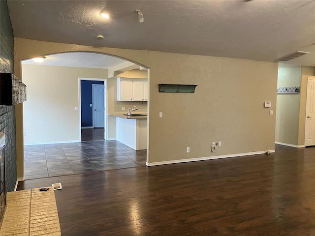 9105 Oak Creek Dr, Midwest City, OK 73130 - unfurnished living room featuring dark wood finished floors, a fireplace, a textured wall, arched walkways, and a textured ceiling