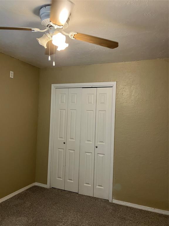 9105 Oak Creek Dr, Midwest City, OK 73130 - unfurnished bedroom featuring dark carpet, a closet, and a ceiling fan