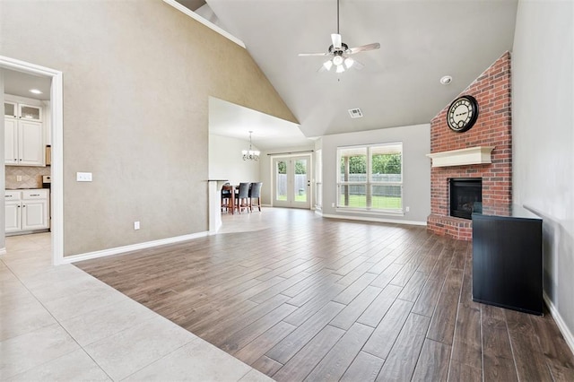 9024 NW 79th Ter, Yukon, OK 73099 - unfurnished living room with high vaulted ceiling, a fireplace, wood finished floors, a ceiling fan, and a chandelier