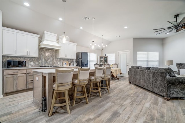 14812 Deerbrook Blvd, Oklahoma City, OK 73142 - kitchen featuring custom exhaust hood, stainless steel microwave, open floor plan, an island with sink, and light wood-type flooring
