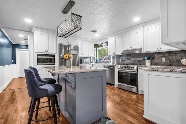 1800 SW 6th St, Ardmore, OK 73401 - kitchen featuring appliances with stainless steel finishes, under cabinet range hood, white cabinets, backsplash, and a kitchen bar