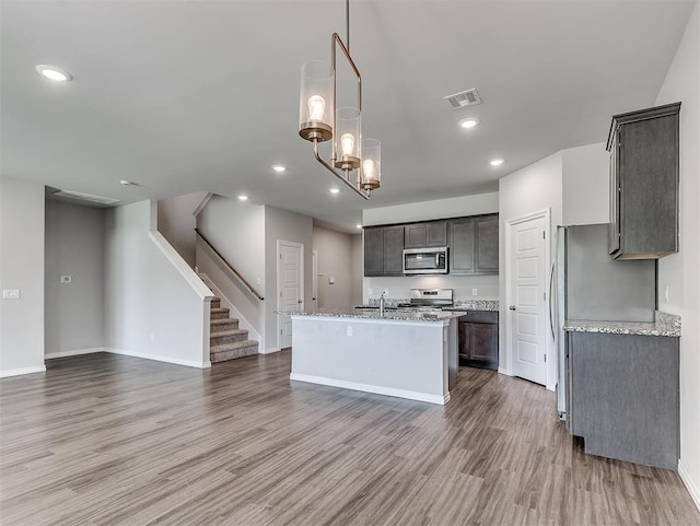 4205 Palmetto Bluff Dr, Mustang, OK 73064 - kitchen with appliances with stainless steel finishes, a center island with sink, wood finished floors, light stone countertops, and recessed lighting