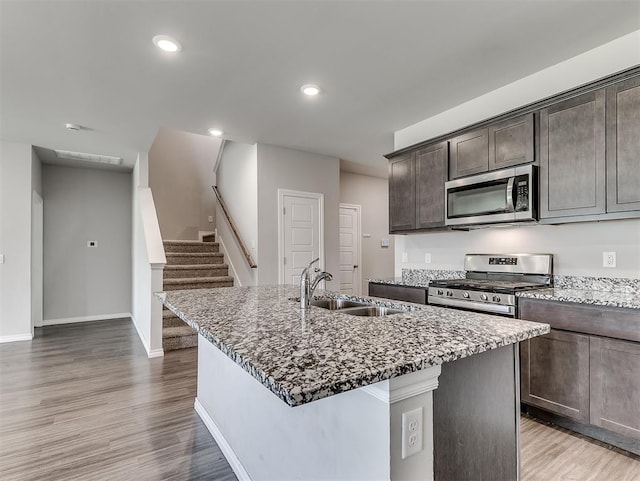 4205 Palmetto Bluff Dr, Mustang, OK 73064 - kitchen featuring stainless steel appliances, dark brown cabinets, a center island with sink, light wood finished floors, and dark stone counters