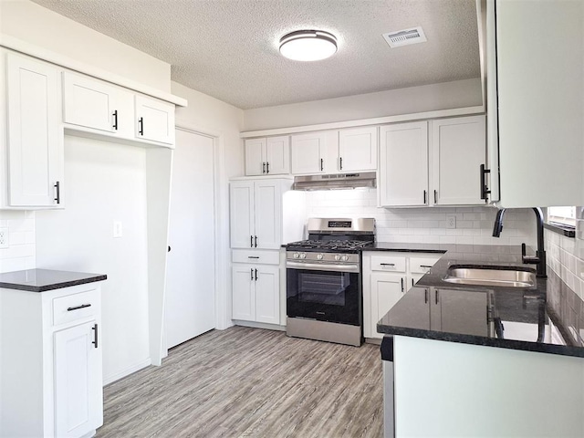 4713 Meench Dr, Del City, OK 73115 - kitchen with stainless steel gas stove, under cabinet range hood, decorative backsplash, white cabinets, and light wood-style floors