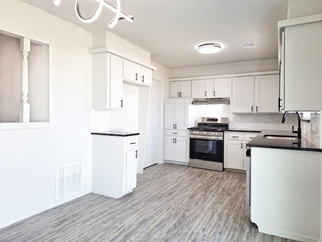 4713 Meench Dr, Del City, OK 73115 - kitchen with stainless steel range with gas stovetop, under cabinet range hood, dark countertops, light wood finished floors, and a textured ceiling
