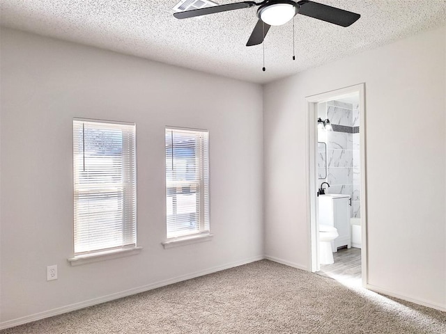 4713 Meench Dr, Del City, OK 73115 - unfurnished bedroom featuring multiple windows, carpet flooring, a textured ceiling, connected bathroom, and a ceiling fan