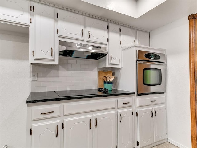 17 Pueblo, Edmond, OK 73013 - kitchen featuring stainless steel oven, black electric cooktop, under cabinet range hood, dark countertops, and decorative backsplash