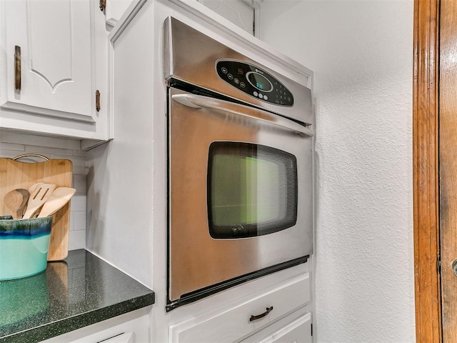 17 Pueblo, Edmond, OK 73013 - kitchen featuring stainless steel oven, white cabinets, a textured wall, dark countertops, and tasteful backsplash