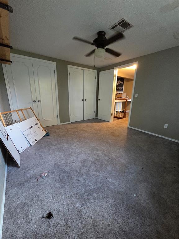 5621 NW 83rd St, Oklahoma City, OK 73132 - unfurnished bedroom featuring a textured ceiling, two closets, ceiling fan, and carpet floors