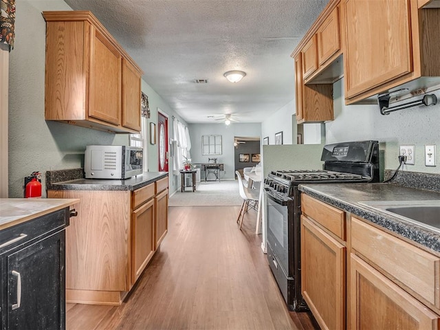 2028 Carlisle Rd, The Village, OK 73120 - kitchen featuring black gas range oven, a ceiling fan, dark countertops, wood finished floors, and a textured ceiling