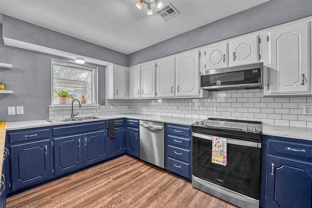 224 N Quail Run, Altus, OK 73521 - kitchen with stainless steel appliances, light wood-type flooring, blue cabinetry, decorative backsplash, and a textured wall