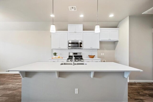 2020 Sara Vista Dr, Yukon, OK 73099 - kitchen featuring appliances with stainless steel finishes, a center island with sink, white cabinets, dark wood-type flooring, and tasteful backsplash