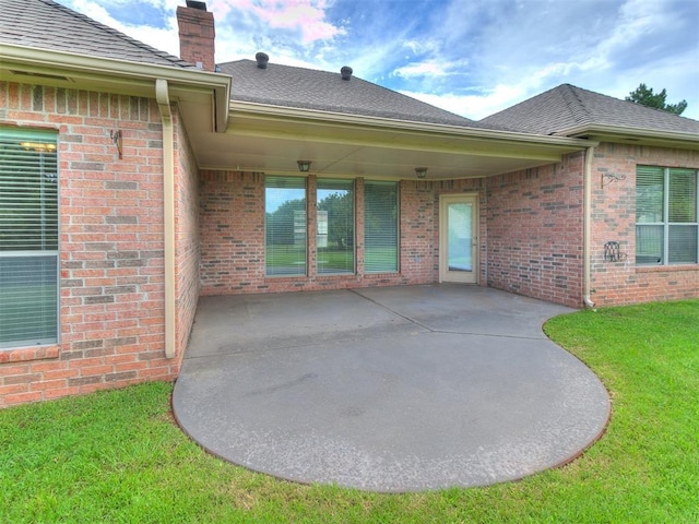 112 Lakeview Ct, Edmond, OK 73003 - rear view of house with a chimney, a patio area, brick siding, a shingled roof, and a lawn