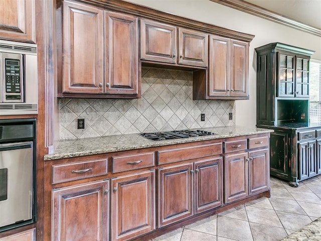 112 Lakeview Ct, Edmond, OK 73003 - kitchen featuring appliances with stainless steel finishes, tasteful backsplash, light stone counters, light tile patterned floors, and crown molding