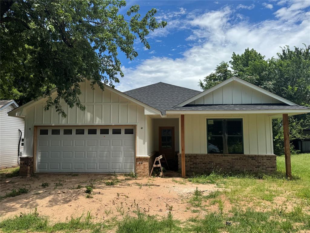 203 W Holly St, Tuttle, OK 73089 - view of front of property featuring brick siding, roof with shingles, a garage, and board and batten siding