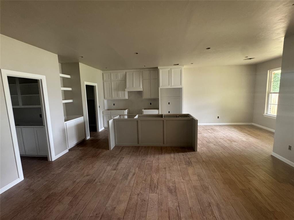 203 W Holly St, Tuttle, OK 73089 - kitchen featuring dark wood finished floors, a center island, built in shelves, and white cabinetry