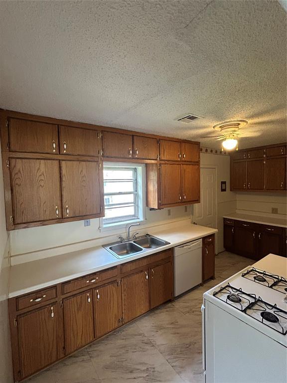 1708 W Modelle Ave, Clinton, OK 73601 - kitchen with white appliances, light marble finish flooring, a textured ceiling, light countertops, and brown cabinetry