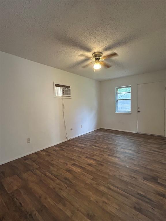 1708 W Modelle Ave, Clinton, OK 73601 - unfurnished room with a textured ceiling, dark wood-style flooring, ceiling fan, and a wall unit AC