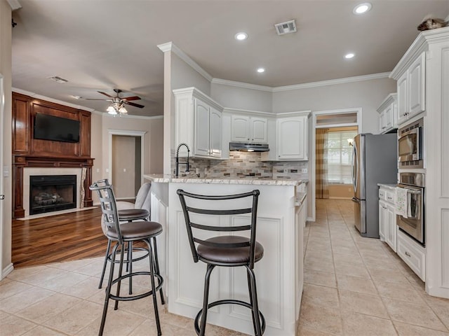 1810 Sandpiper Dr, Blanchard, OK 73010 - kitchen with stainless steel appliances, a peninsula, a ceiling fan, under cabinet range hood, and light tile patterned floors
