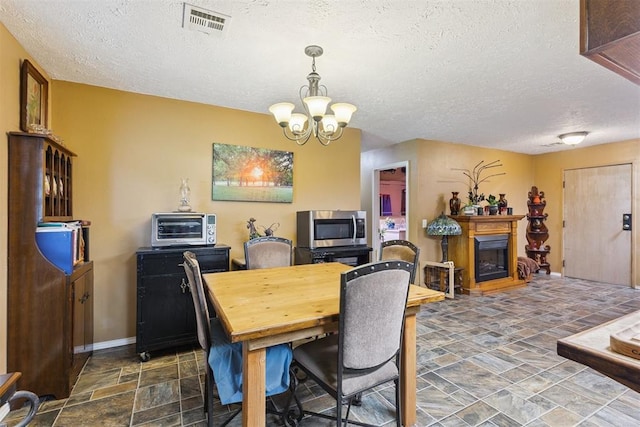 349760 E 970th Rd, Sparks, OK 74869 - dining room featuring stone finish floors, a textured ceiling, a chandelier, and a fireplace with raised hearth