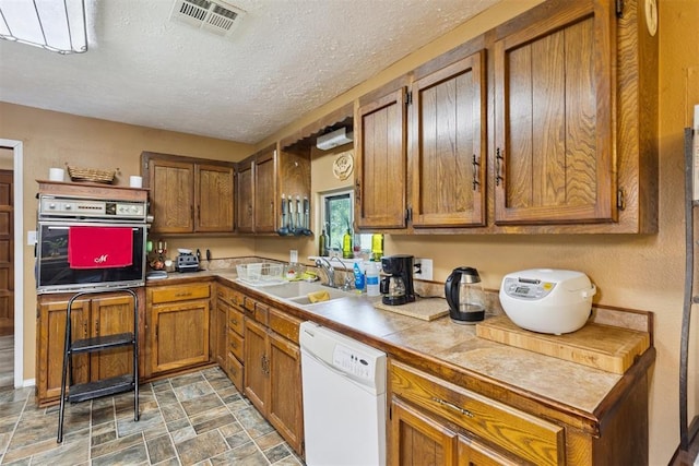 349760 E 970th Rd, Sparks, OK 74869 - kitchen with wall oven, dishwasher, brown cabinetry, stone finish floors, and a textured ceiling