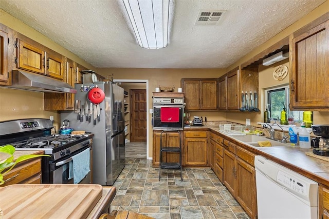 349760 E 970th Rd, Sparks, OK 74869 - kitchen with appliances with stainless steel finishes, under cabinet range hood, brown cabinets, stone finish flooring, and a textured ceiling