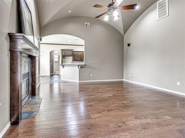 2311 Washita Trl, Edmond, OK 73003 - unfurnished living room featuring arched walkways, ceiling fan, a fireplace, dark wood-type flooring, and vaulted ceiling