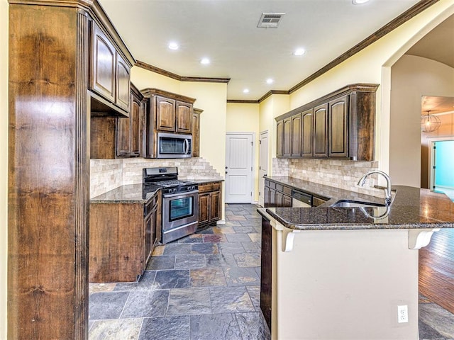 2311 Washita Trl, Edmond, OK 73003 - kitchen with stainless steel appliances, crown molding, dark stone countertops, a peninsula, and decorative backsplash