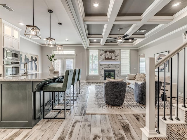 15913 Windrush Pl, Edmond, OK 73013 - living area with a ceiling fan, light wood-style flooring, healthy amount of natural light, a large fireplace, and ornamental molding