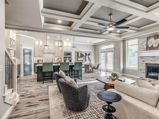 15913 Windrush Pl, Edmond, OK 73013 - living room featuring light wood-style floors, ceiling fan, crown molding, a fireplace, and coffered ceiling