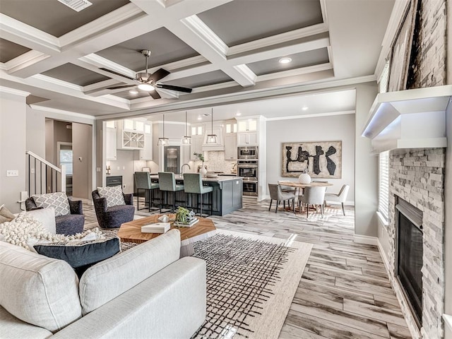 15913 Windrush Pl, Edmond, OK 73013 - living room featuring ornamental molding, a fireplace, coffered ceiling, a ceiling fan, and beam ceiling