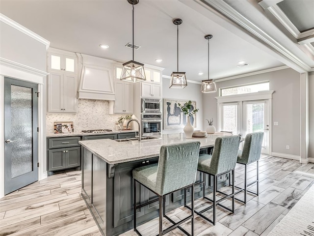 15913 Windrush Pl, Edmond, OK 73013 - kitchen with stainless steel appliances, custom range hood, gray cabinets, ornamental molding, and a kitchen island with sink