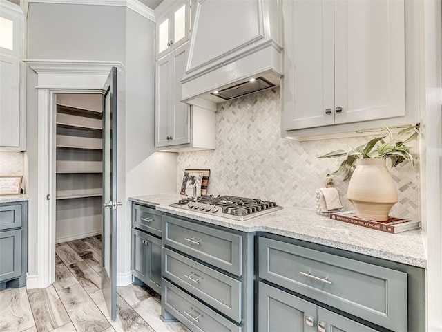 15913 Windrush Pl, Edmond, OK 73013 - kitchen with stainless steel gas cooktop, gray cabinets, backsplash, light stone counters, and custom exhaust hood