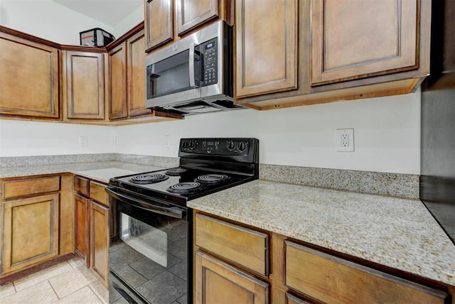 13664 NW Bradbury Ln, Piedmont, OK 73078 - kitchen featuring black electric range, stainless steel microwave, light tile patterned floors, and brown cabinets
