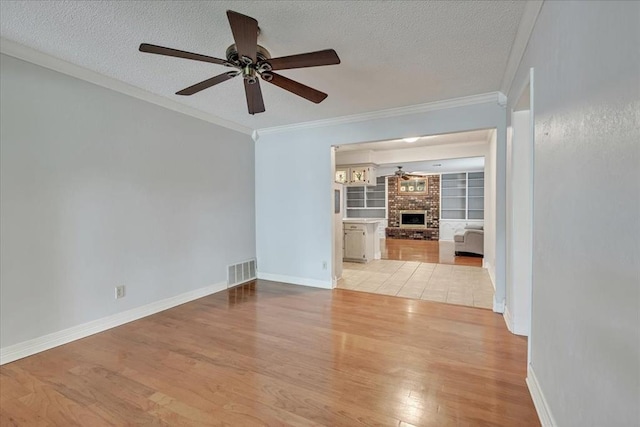 829 Arnold Ave, Moore, OK 73160 - empty room featuring a ceiling fan, wood finished floors, a textured ceiling, ornamental molding, and a brick fireplace