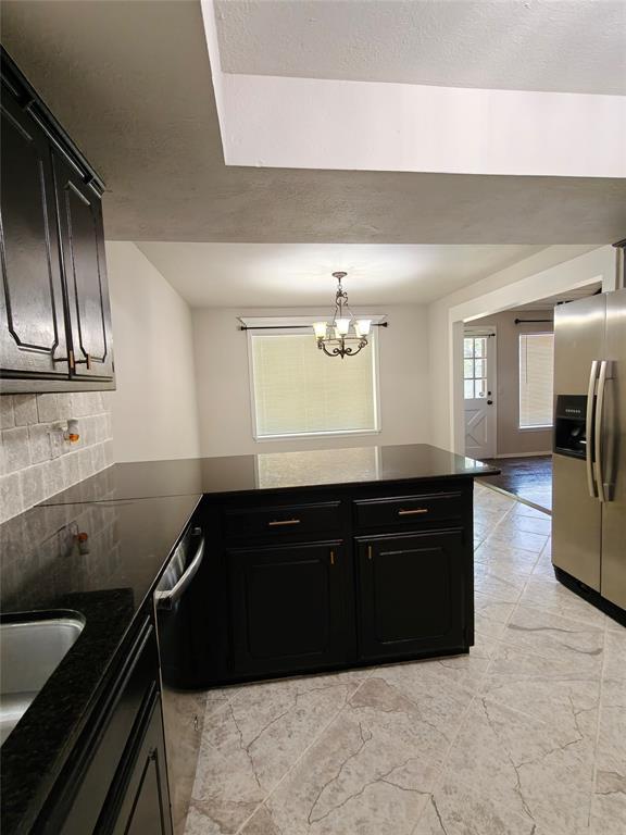 11208 NW 113th St, Yukon, OK 73099 - kitchen with stainless steel appliances, dark cabinetry, a chandelier, a peninsula, and decorative backsplash