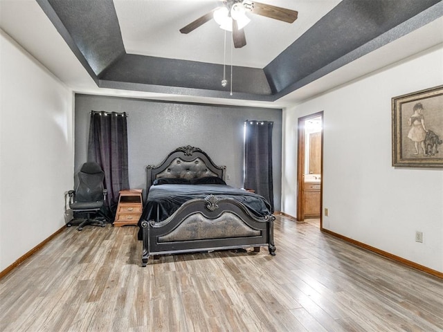 6708 Basswood Canyon Rd, Oklahoma City, OK 73162 - bedroom featuring a raised ceiling, wood finished floors, connected bathroom, and a ceiling fan
