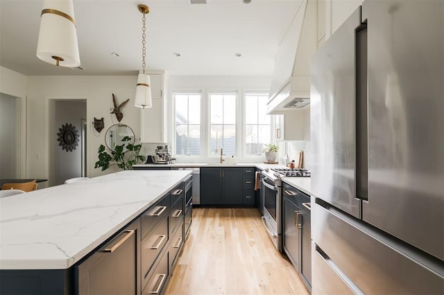 1900 Runway Blvd, Oklahoma City, OK 73108 - kitchen with appliances with stainless steel finishes, custom range hood, light wood finished floors, a center island, and hanging light fixtures