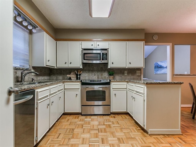 1221 Val Genes Rd, Edmond, OK 73003 - kitchen featuring stainless steel appliances, tasteful backsplash, a peninsula, white cabinetry, and a textured ceiling