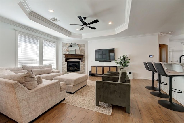 15728 Egerton Pl, Edmond, OK 73013 - living room with ceiling fan, a tray ceiling, ornamental molding, light wood-type flooring, and a fireplace