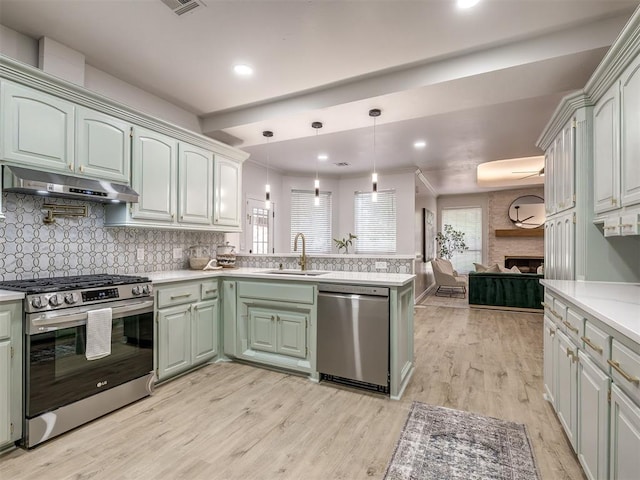 1340 NW 168th St, Edmond, OK 73012 - kitchen featuring appliances with stainless steel finishes, under cabinet range hood, a peninsula, a fireplace, and plenty of natural light