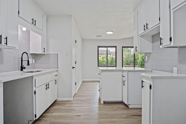3300 Outpost Cir, Norman, OK 73072 - kitchen featuring decorative backsplash, light wood-style flooring, light countertops, a textured ceiling, and white cabinets