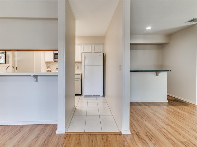 4400 Hemingway Dr Unit 221, Oklahoma City, OK 73118 - kitchen featuring freestanding refrigerator, a breakfast bar, light wood-type flooring, white cabinetry, and recessed lighting