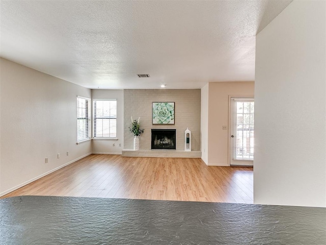 4400 Hemingway Dr Unit 221, Oklahoma City, OK 73118 - unfurnished living room with wood finished floors, plenty of natural light, a textured ceiling, and a brick fireplace