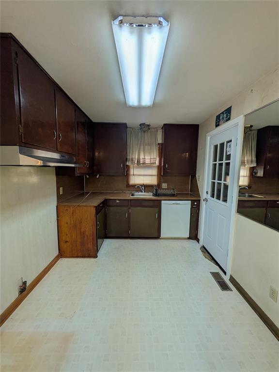 733 E Steed Dr, Midwest City, OK 73110 - kitchen featuring dishwasher, under cabinet range hood, dark brown cabinetry, and light floors